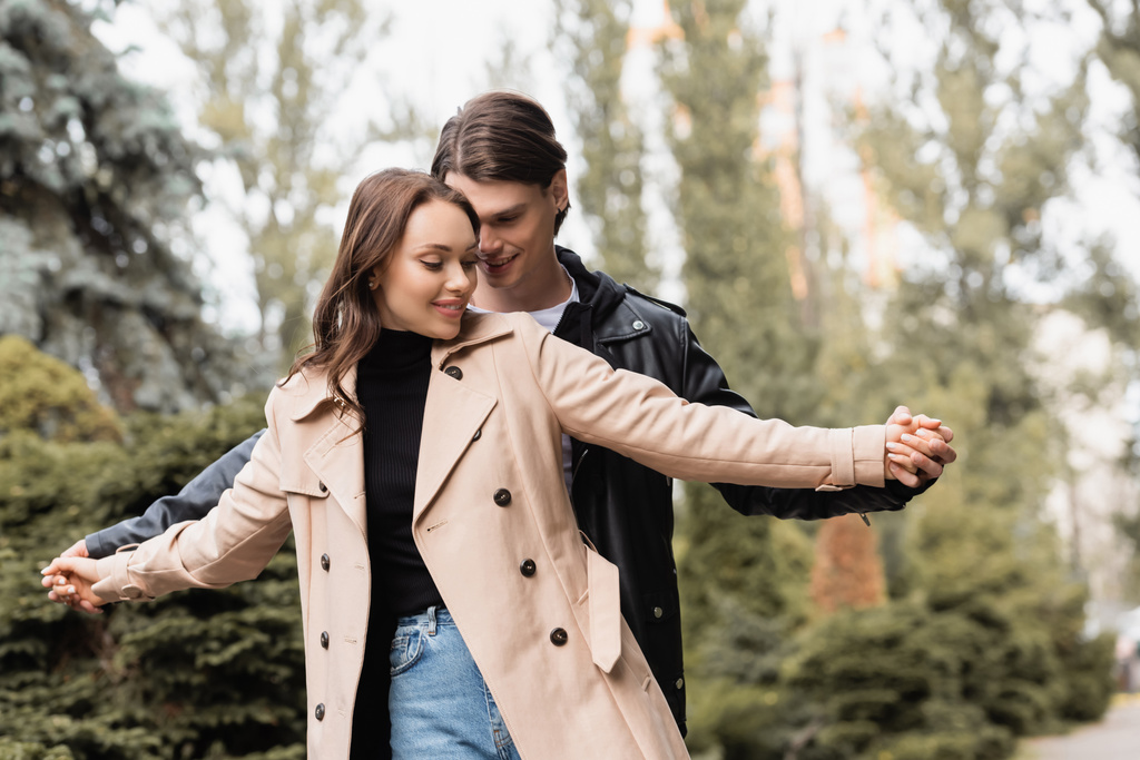 homme joyeux tenant la main avec petite amie heureuse en trench coat beige  - Photo, image