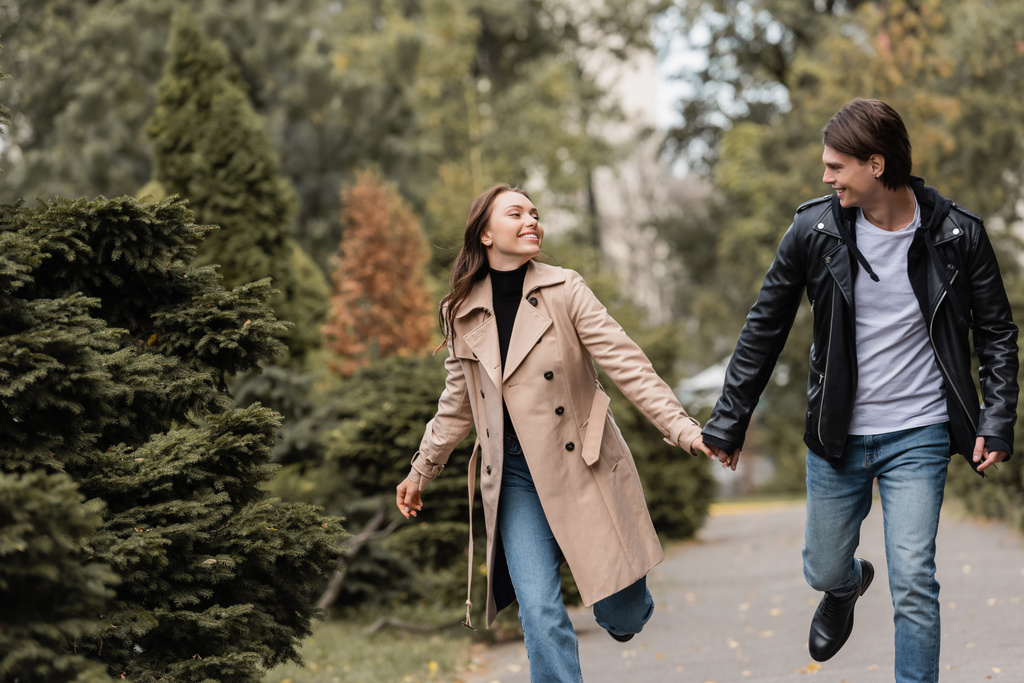 vidám és stílusos pár őszi ruhákban kéz a kézben sétálva a parkban  - Fotó, kép