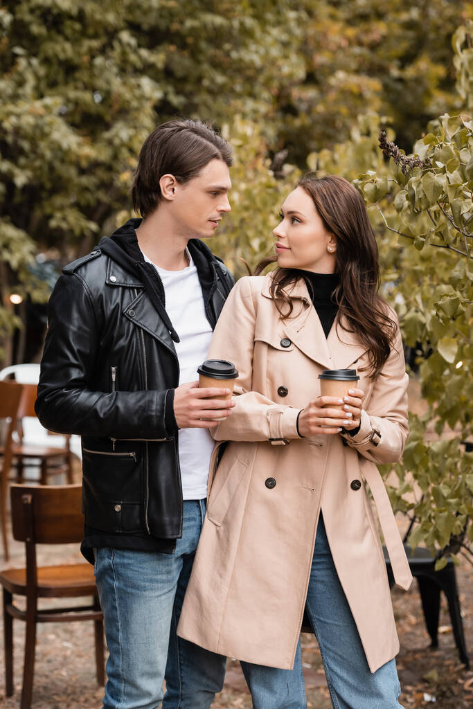молода жінка і чоловік в стильному вбранні тримають каву, щоб піти і дивитися один на одного
 - Фото, зображення