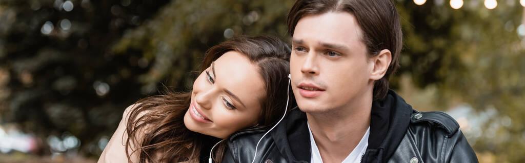 wesoła kobieta i młody mężczyzna dzielą słuchawki przewodowe podczas słuchania muzyki razem, baner - Zdjęcie, obraz