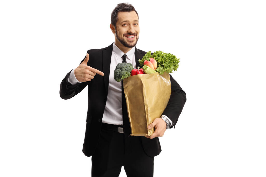 Młody biznesmen trzymający papierową torbę z zakupami i wskazujący odizolowany na białym tle - Zdjęcie, obraz