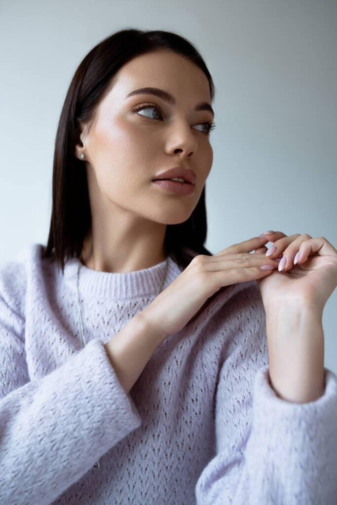 jolie femme brune avec un maquillage naturel portant un pull tricoté et regardant loin isolé sur gris - Photo, image