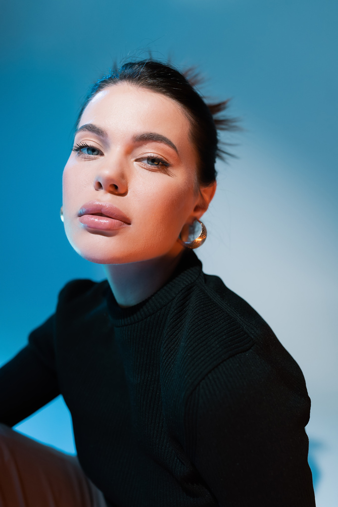 портрет женщины с натуральным макияжем в черном свитере на синем фоне - Фото, изображение