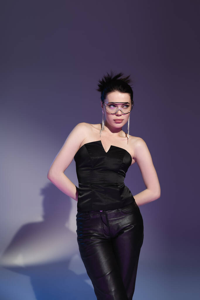 ブルネット女性でファッショナブルな眼鏡と黒コルセットで手で後ろと離れて紫色の背景を見ます - 写真・画像