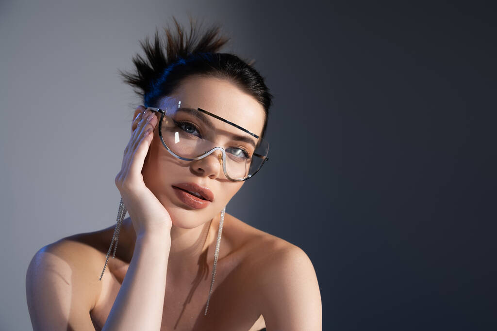 Portrait of stylish woman with naked shoulders and sunglasses looking at camera on grey background  - Photo, Image