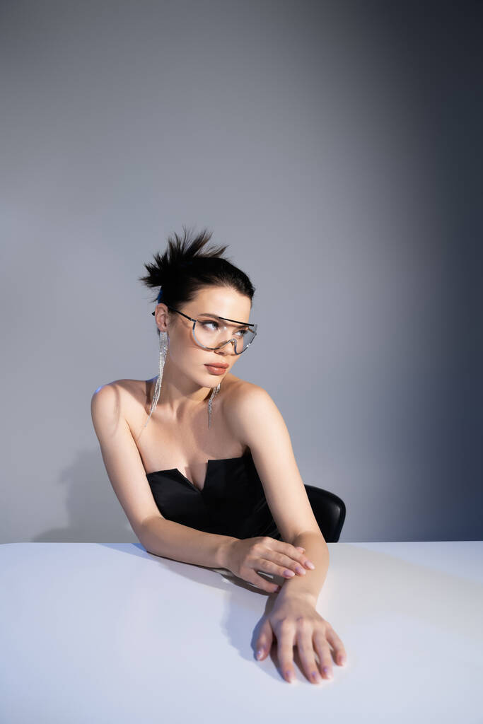 Stylish woman in black corset and sunglasses posing near table on grey background  - Photo, Image