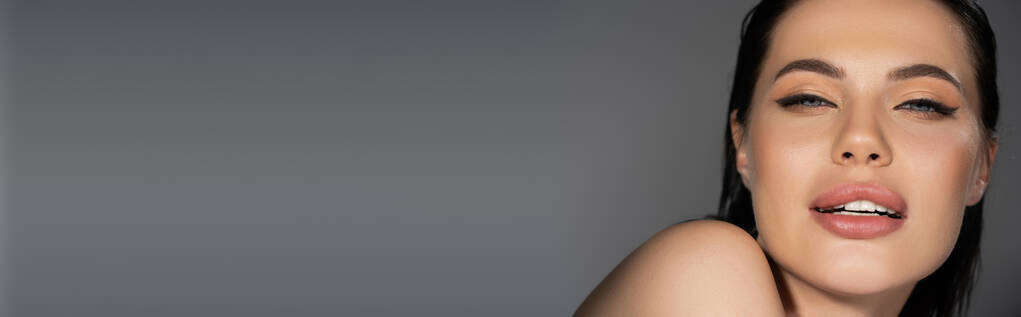 Junge Frau mit Make-up und nackter Schulter blickt vereinzelt in die Kamera auf grauem Banner  - Foto, Bild