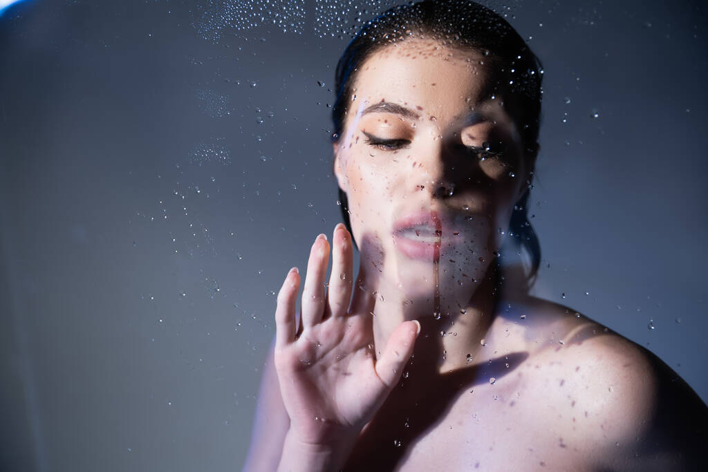fiatal nő meztelen vállak nézi nedves üveg szürke háttér  - Fotó, kép