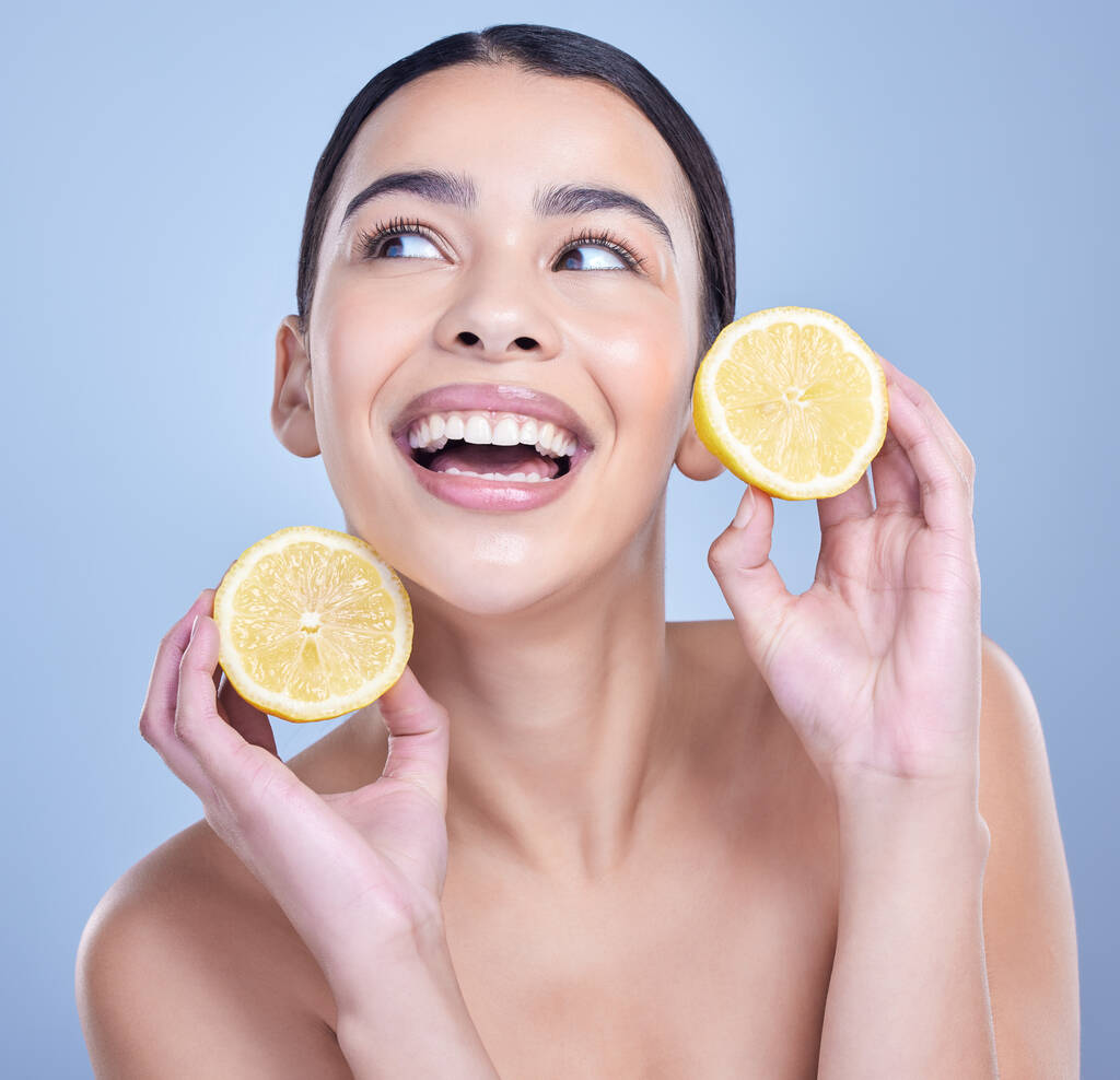 A happy smiling mixed race woman holding a lemon. Hispanic model promoting the skin benefits of a healthy diet against a blue copyspace background. - Фото, изображение