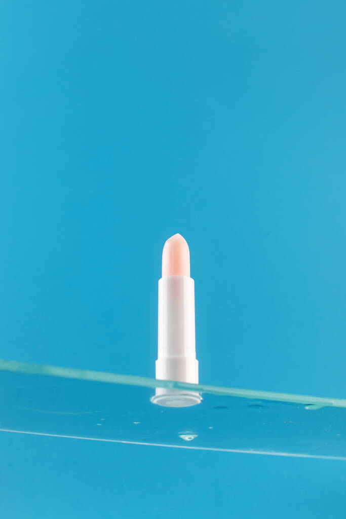  Rouge à lèvres hygiénique rose hydratant sur une étagère en verre sur un fond bleu. Concept de soins de la peau. - Photo, image