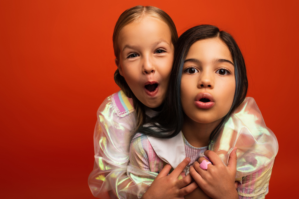 αστεία προεφηβικά κορίτσια κοιτάζοντας κάμερα και γκρίνια με ανοιχτά στόματα απομονώνονται σε πορτοκαλί - Φωτογραφία, εικόνα