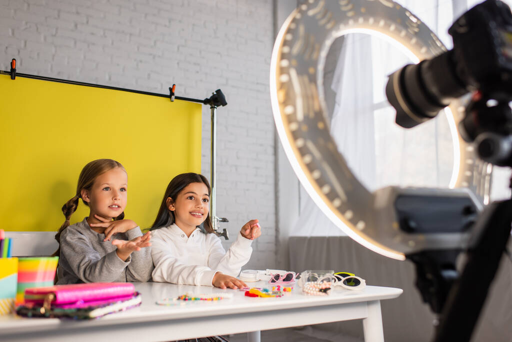preteen bloggers talking near different accessories on table near digital camera with ring light on blurred foreground - Photo, Image