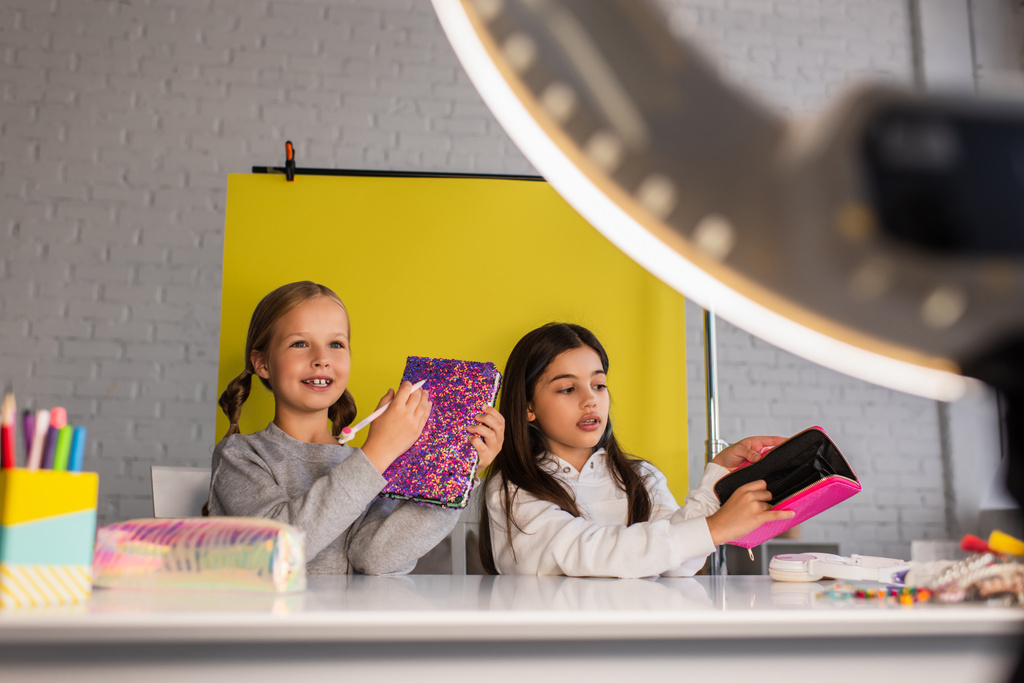 tiener video bloggers tonen schoolbenodigdheden op gele achtergrond in de voorkant van wazig cirkel lamp - Foto, afbeelding