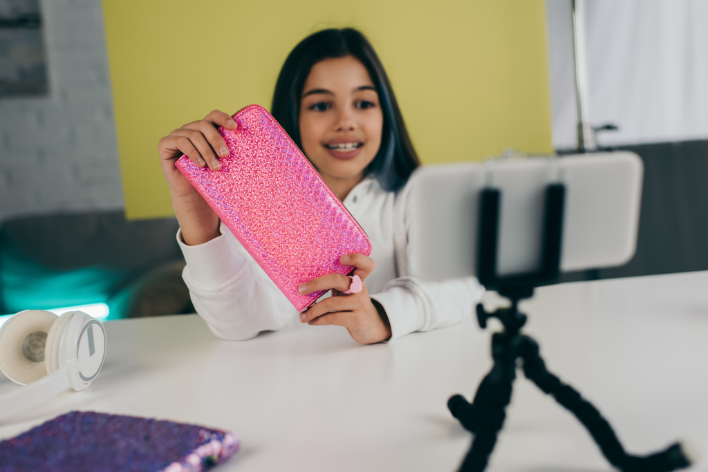 sorrindo menina borrada mostrando caso lápis brilhante perto do smartphone no suporte do telefone - Foto, Imagem
