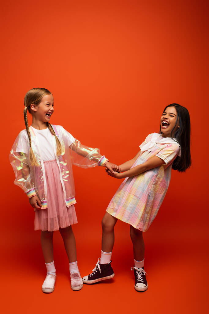 збуджена брюнетка дівчина тримає руку друга і сміється на помаранчевому фоні
 - Фото, зображення