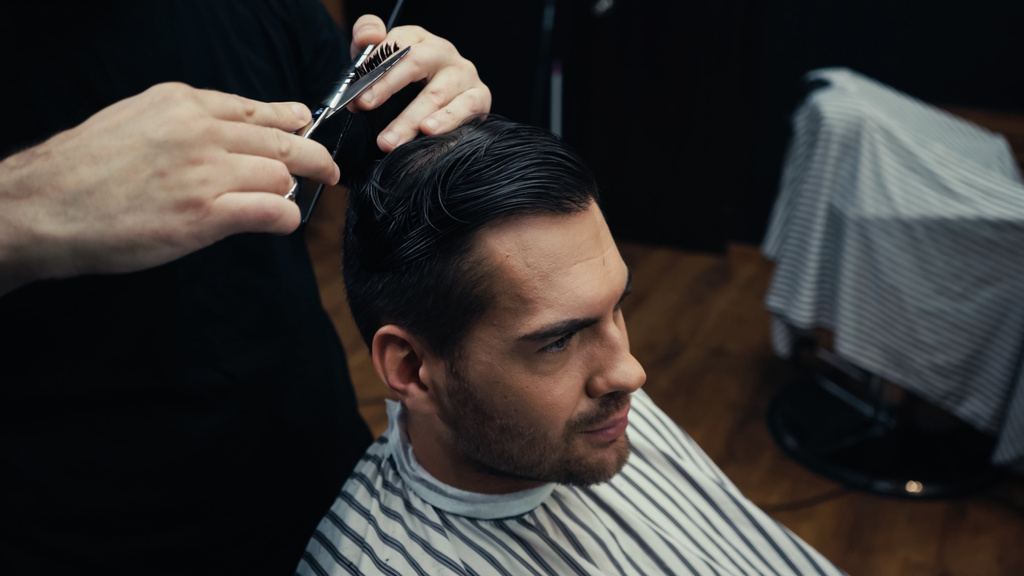 Fryzjer obcinanie włosów człowieka w pelerynie fryzjerskiej w salonie  - Zdjęcie, obraz