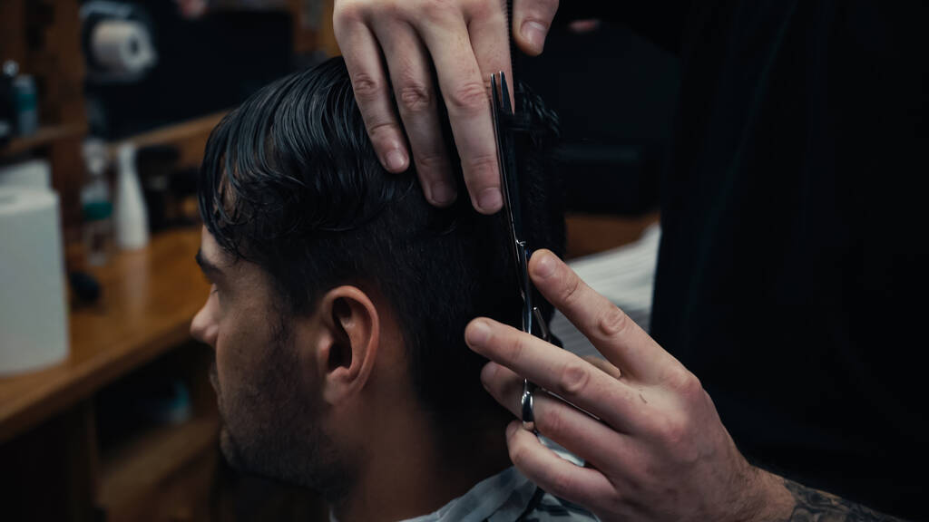 Tätowierte Friseurin schneidet in verschwommenem Friseurladen Haare einer Kundin  - Foto, Bild