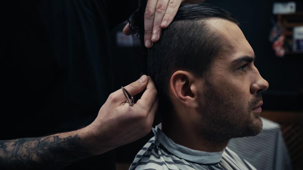 Parrucchiere che tiene forbici e pettinando capelli di uomo in parrucchiere cape in salone  - Foto, immagini