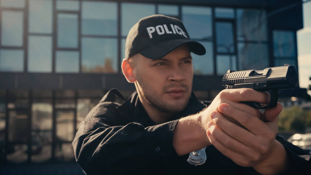 Policeman in uniform and cap holding gun on urban street  - Photo, Image