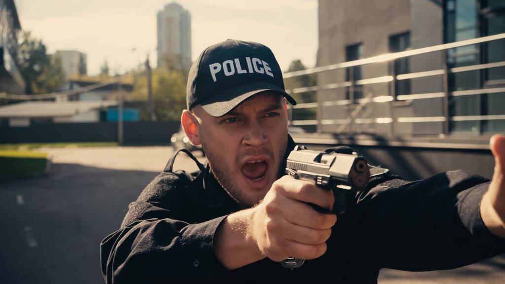 mladý policista v uniformě a čepice drží zbraň při křiku na městské ulici  - Fotografie, Obrázek