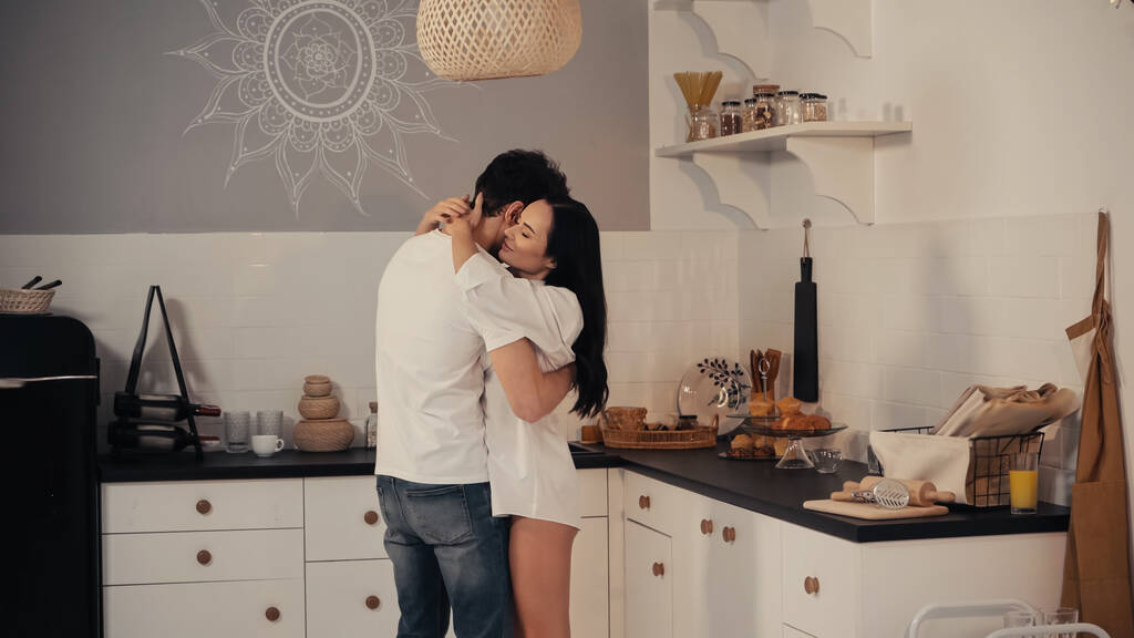Modern mutfakta beyaz gömlekli mutlu kadın erkek arkadaşını kucaklıyor. - Fotoğraf, Görsel