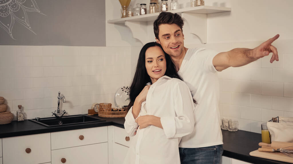 boldog férfi átöleli barátnő és ujjal mutogatás a konyhában - Fotó, kép