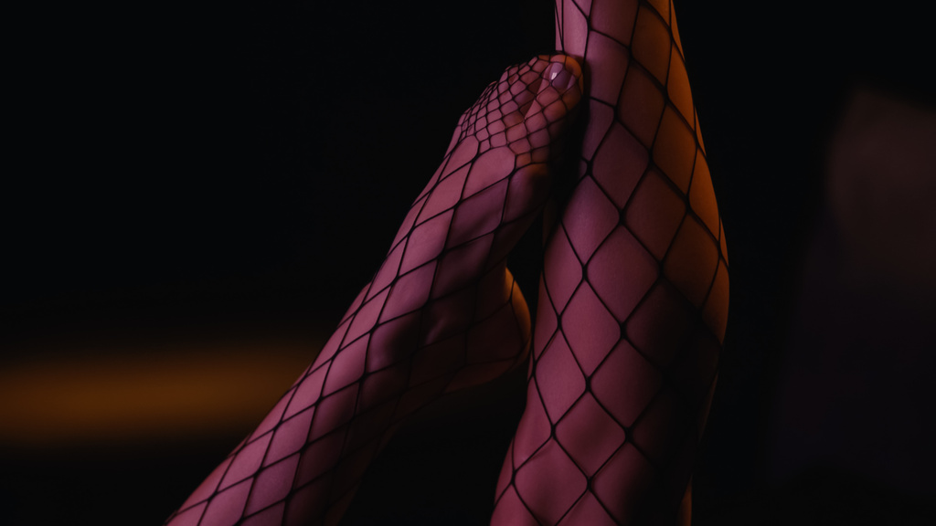 Oříznutý pohled na nohy ženy v síťovaných punčocháče na černém pozadí  - Fotografie, Obrázek