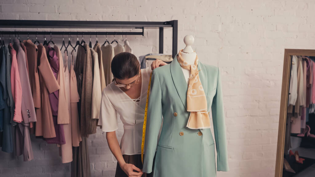 Diseñador que mide la chaqueta elegante en el maniquí en el taller  - Foto, Imagen