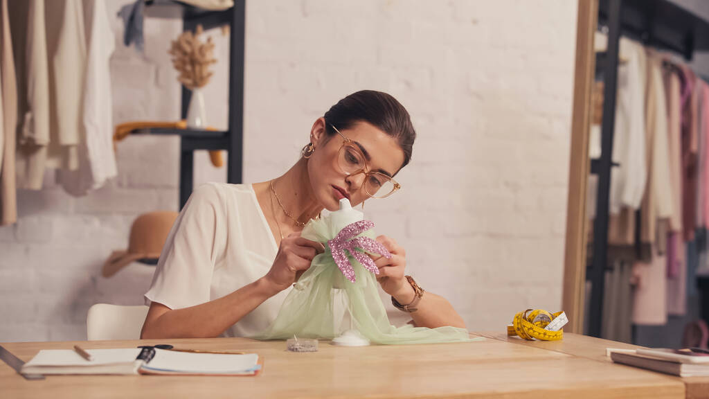 Σχεδιαστής κάνοντας φόρεμα σε μικρό κούκλα κοντά σημειωματάρια στο ατελιέ  - Φωτογραφία, εικόνα