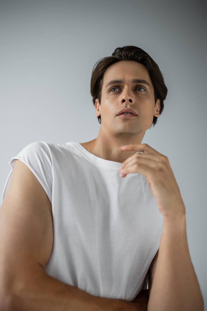 retrato del hombre de ensueño en camiseta blanca mirando hacia otro lado aislado en gris - Foto, Imagen