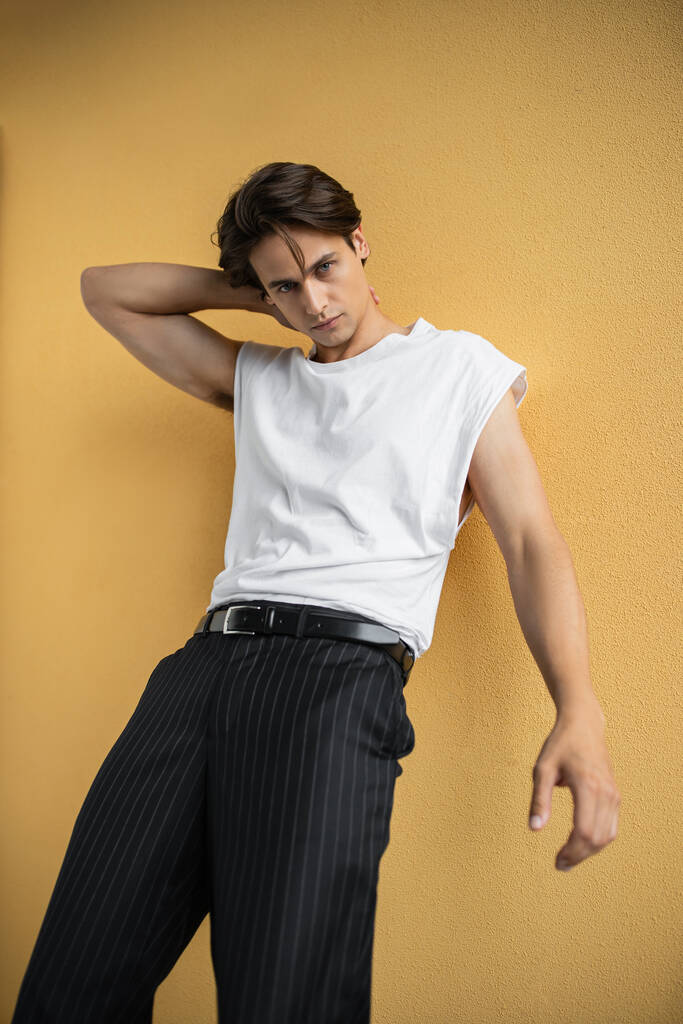 stylish man in white t-shirt and striped trousers posing near yellow wall  - Photo, Image