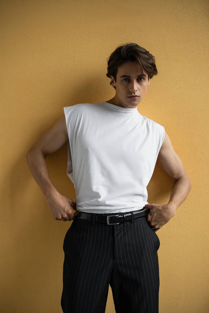 стильний чоловік у білій футболці та смугастих штанях, що стоять біля жовтої стіни
  - Фото, зображення