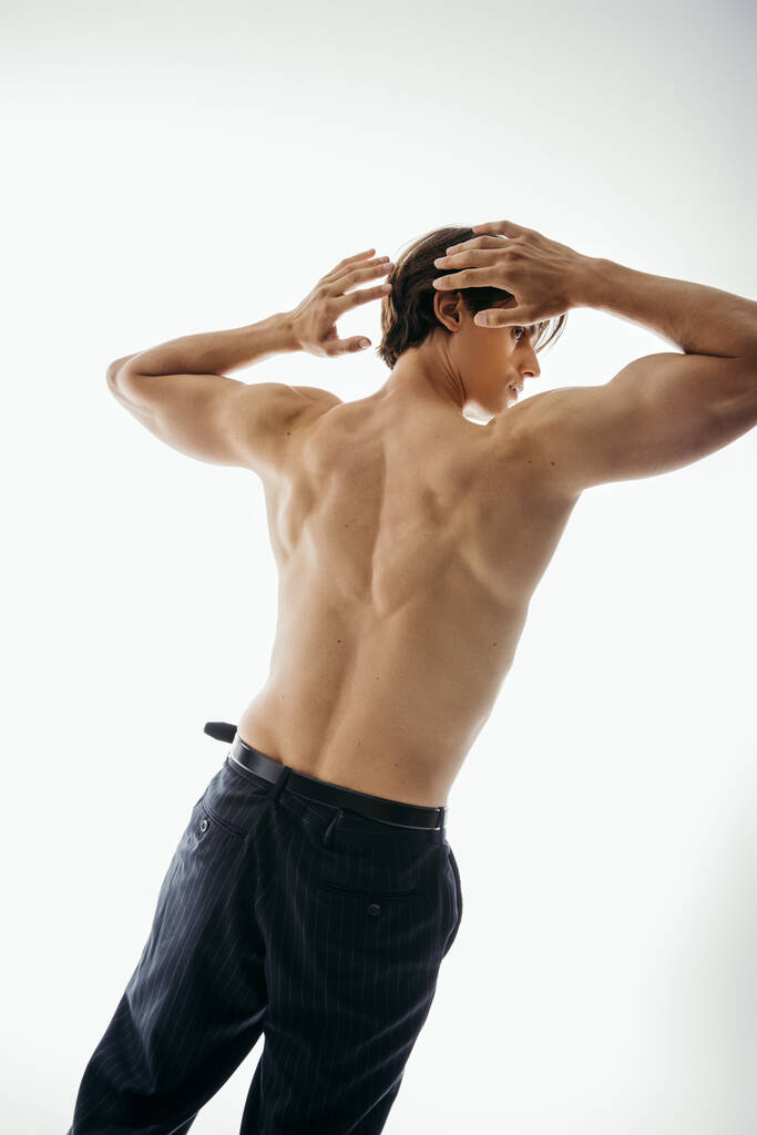 vista lateral do homem muscular e sem camisa em calças pretas olhando para longe no branco - Foto, Imagem