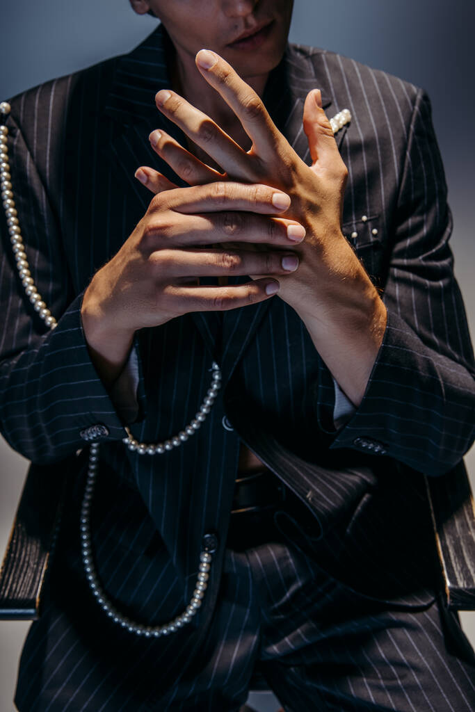 обрізаний вид стильного чоловіка в модному костюмі з перловим ланцюгом жестом на темно-сірому
  - Фото, зображення