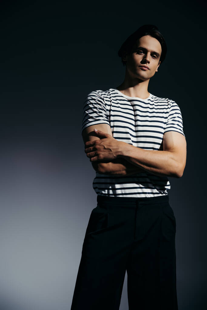 Trendy uomo in t-shirt a righe incrociate braccia su fondo grigio con illuminazione  - Foto, immagini