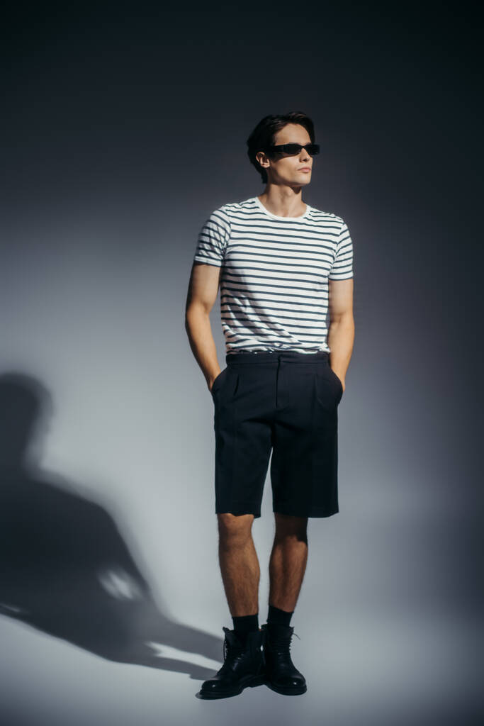 Полная длина стильный человек в шортах и сапогах на сером фоне с тенью  - Фото, изображение