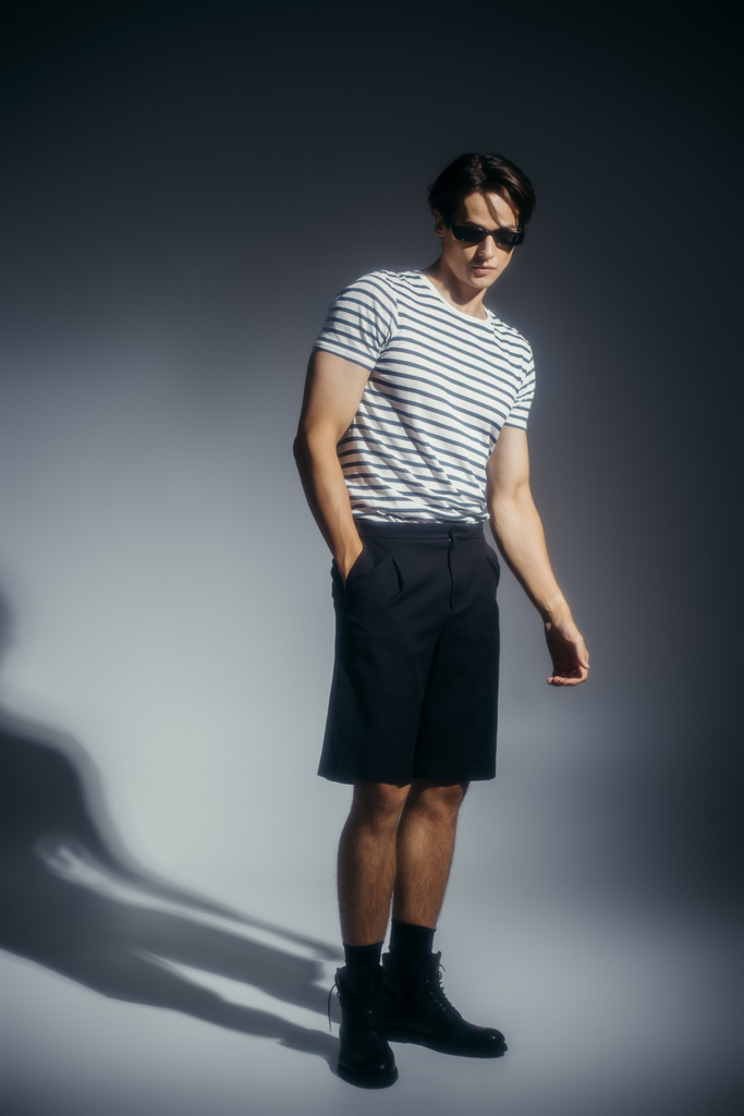 Modelo de moda en gafas de sol y botas sobre fondo gris con sombra  - Foto, Imagen