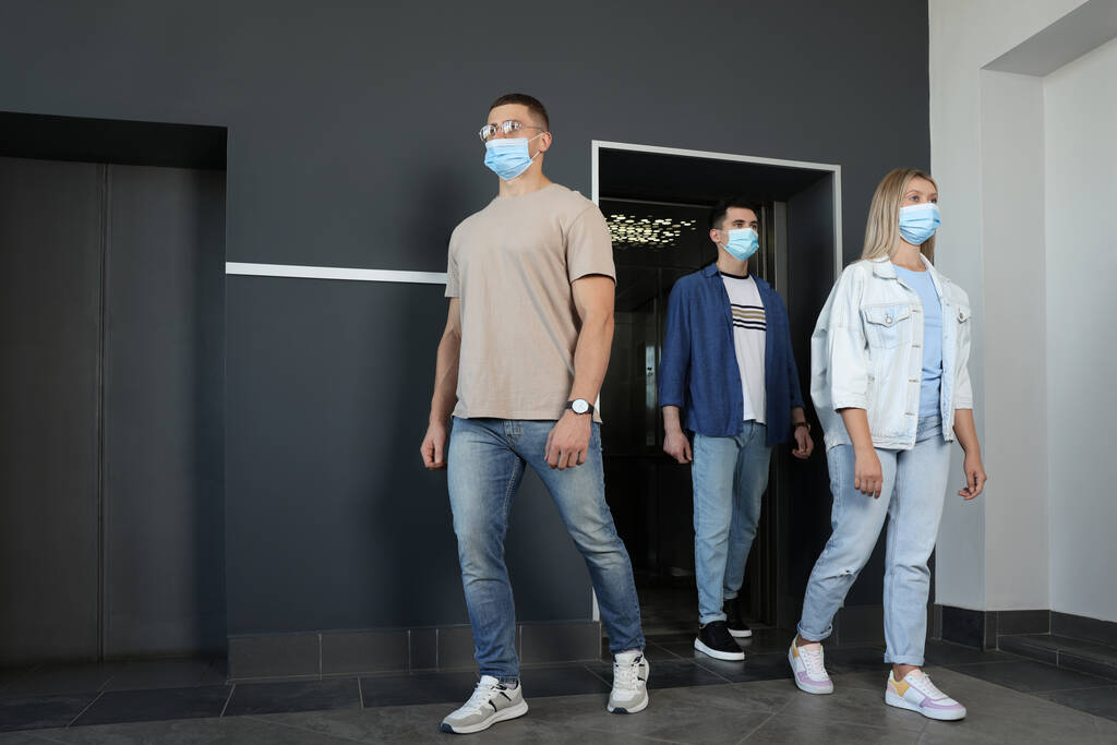 Gruppe von Menschen mit Gesichtsmasken, die aus dem Aufzug gehen. Schutzmaßnahme - Foto, Bild