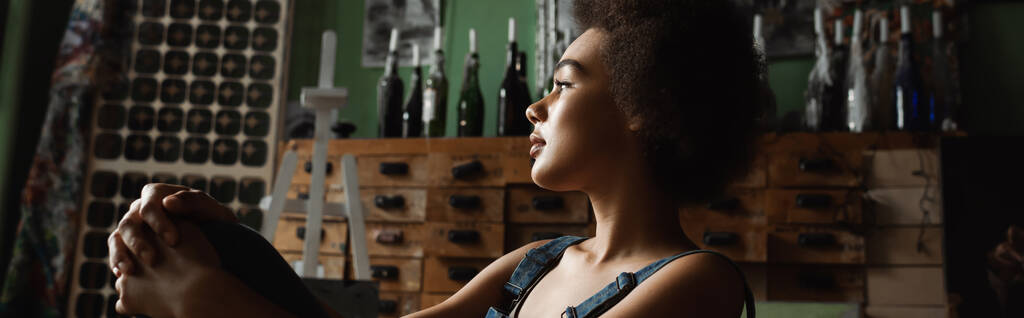 Profil der nachdenklichen afrikanisch-amerikanischen Frau, die in der Werkstatt sitzt und wegschaut, Banner - Foto, Bild