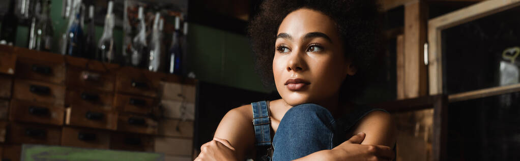 jovem e sonhadora mulher afro-americana sentada em oficina de arte e olhando para longe, banner - Foto, Imagem