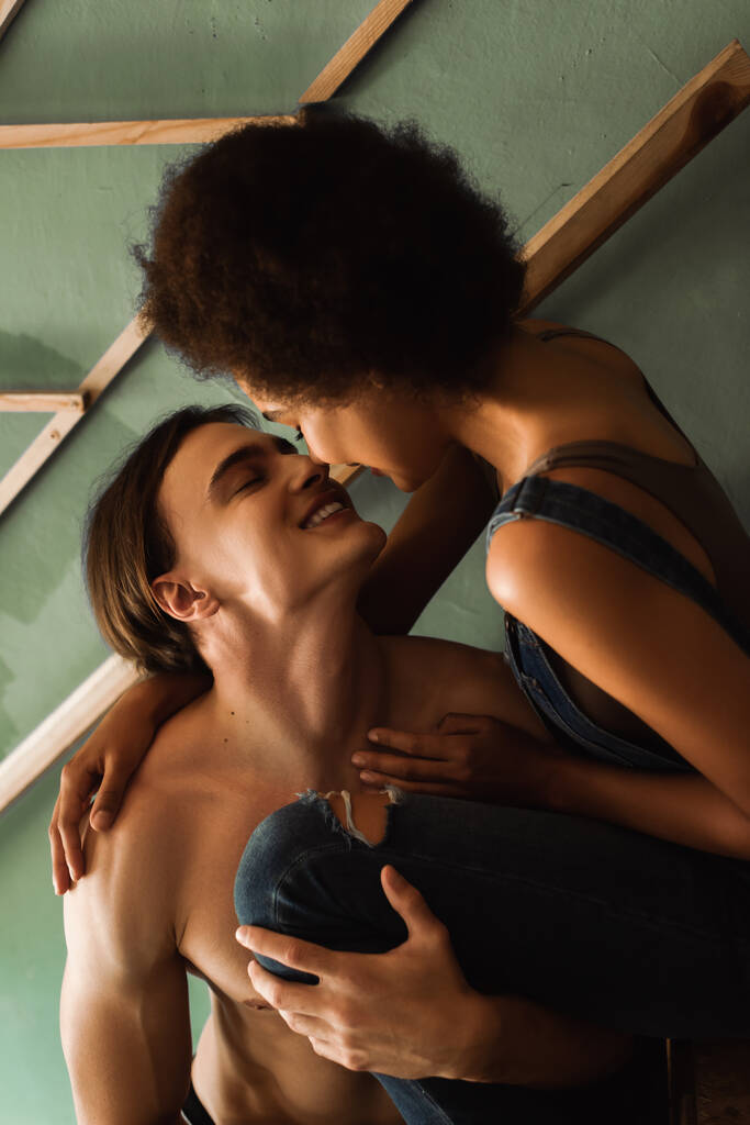 feliz artista sem camisa sorrindo perto sedutor afro-americano namorada em estúdio - Foto, Imagem