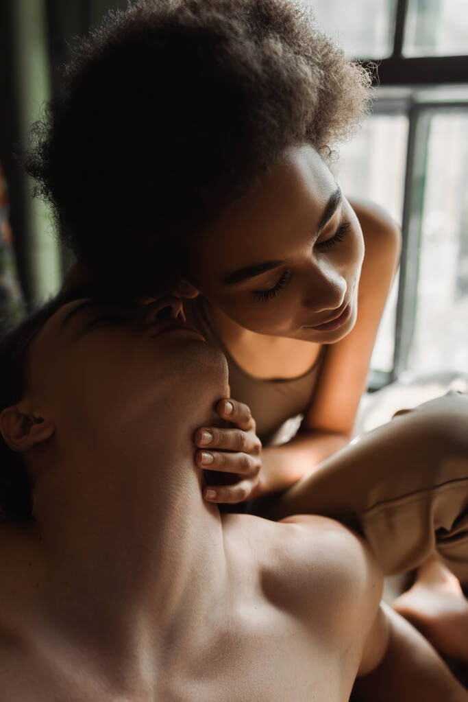 séduisante femme afro-américaine aux yeux fermés près de l'homme torse nu dans un atelier d'art - Photo, image