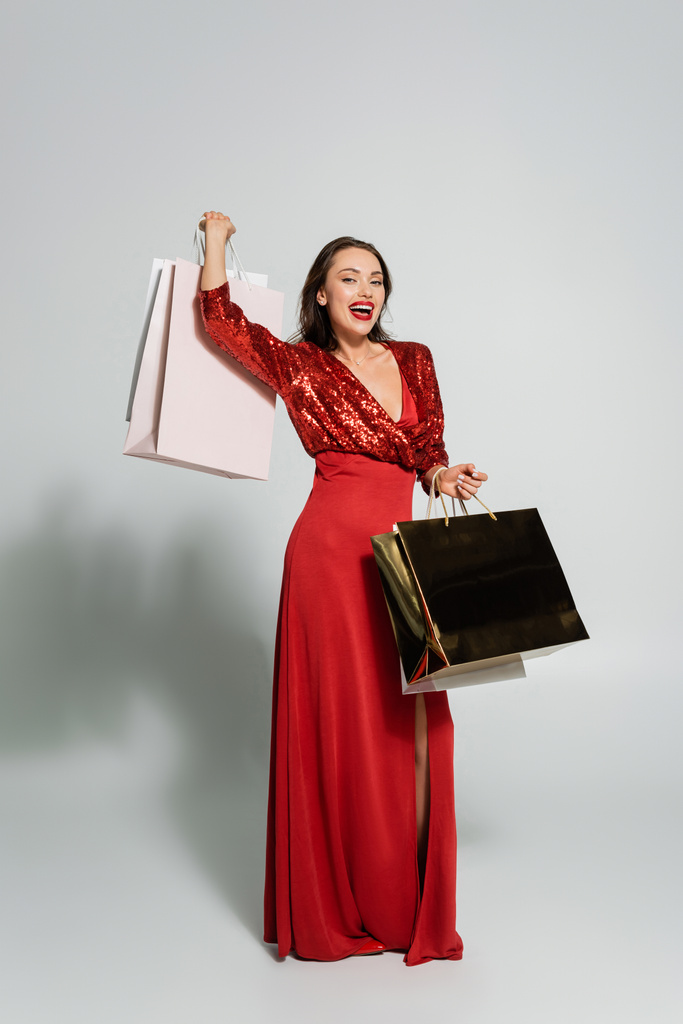 Lunghezza completa della donna elegante in abito rosso che tiene acquisti su sfondo grigio  - Foto, immagini