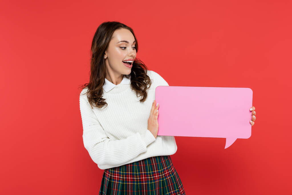 Happy woman in sweater looking at empty speech bubble isolated on red  - Photo, Image