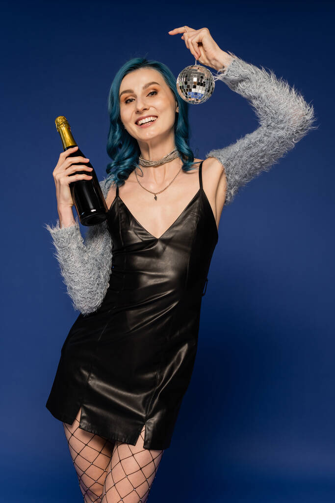 glückliche Frau im schwarzen Lederkleid mit Champagnerflasche und glänzender Discokugel auf blauem Grund - Foto, Bild