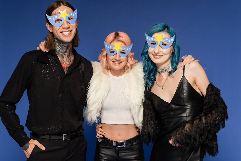 tatuoitu ei-binary henkilö seisoo käsi taskussa lähellä iloinen queer ystäviä puolue naamarit eristetty sininen - Valokuva, kuva