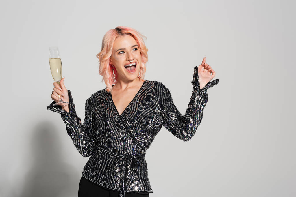 вражена і стильна жінка з келихом шампанського дивиться вбік і вказує пальцем на сірий фон
 - Фото, зображення
