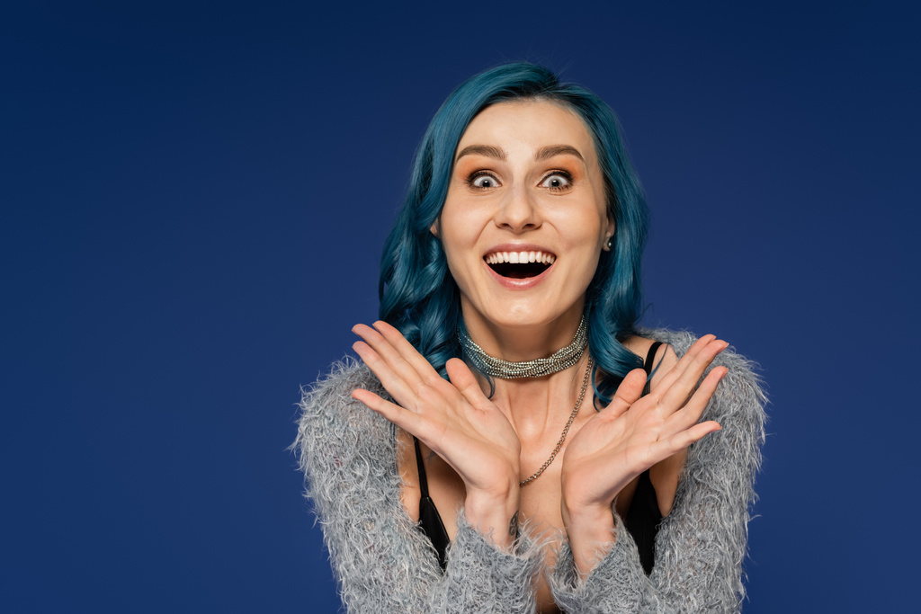 užaslá žena s barevnými vlasy ukazující wow gesto a při pohledu na kameru izolované na modré - Fotografie, Obrázek