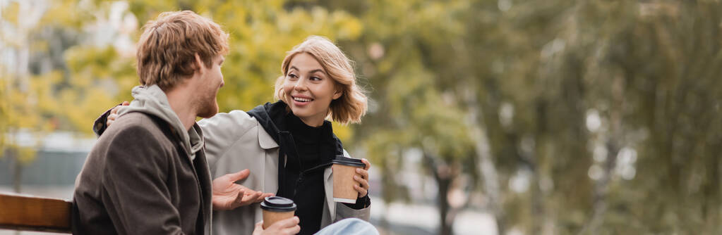 usmívající se mladý pár chatování a drží papírové kelímky s kávou jít, banner - Fotografie, Obrázek