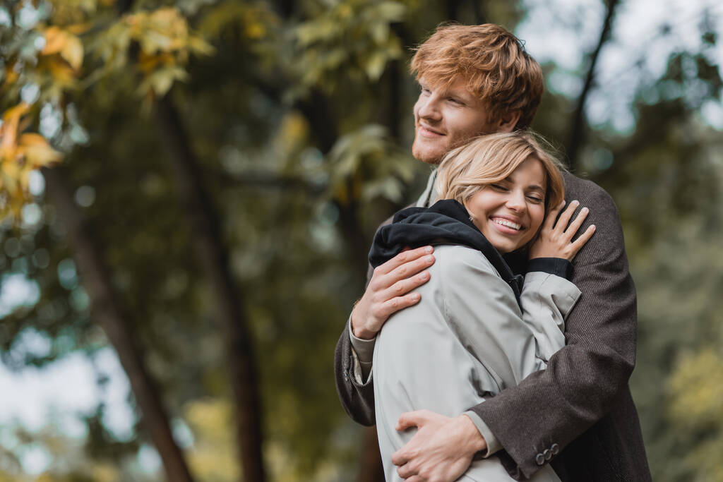 glückliches junges Paar in herbstlichen Mänteln umarmt sich beim Date - Foto, Bild